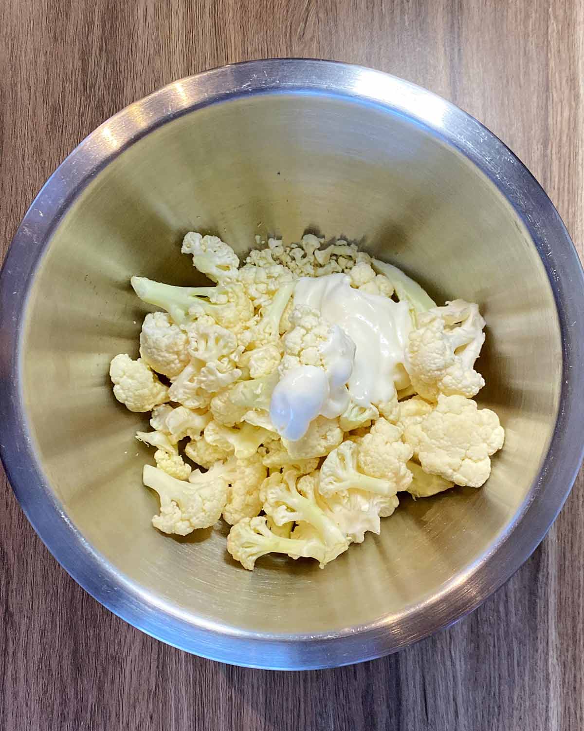 Cauliflower florets and a dollop of mayonsaise in a mixing bowl.