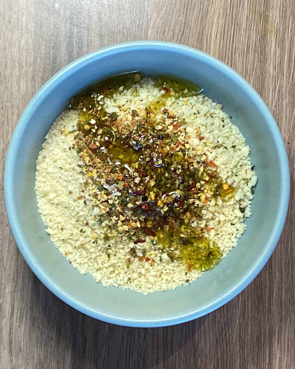 A bowl containing breadcrumbs, grated parmesan, seasoning and oil.