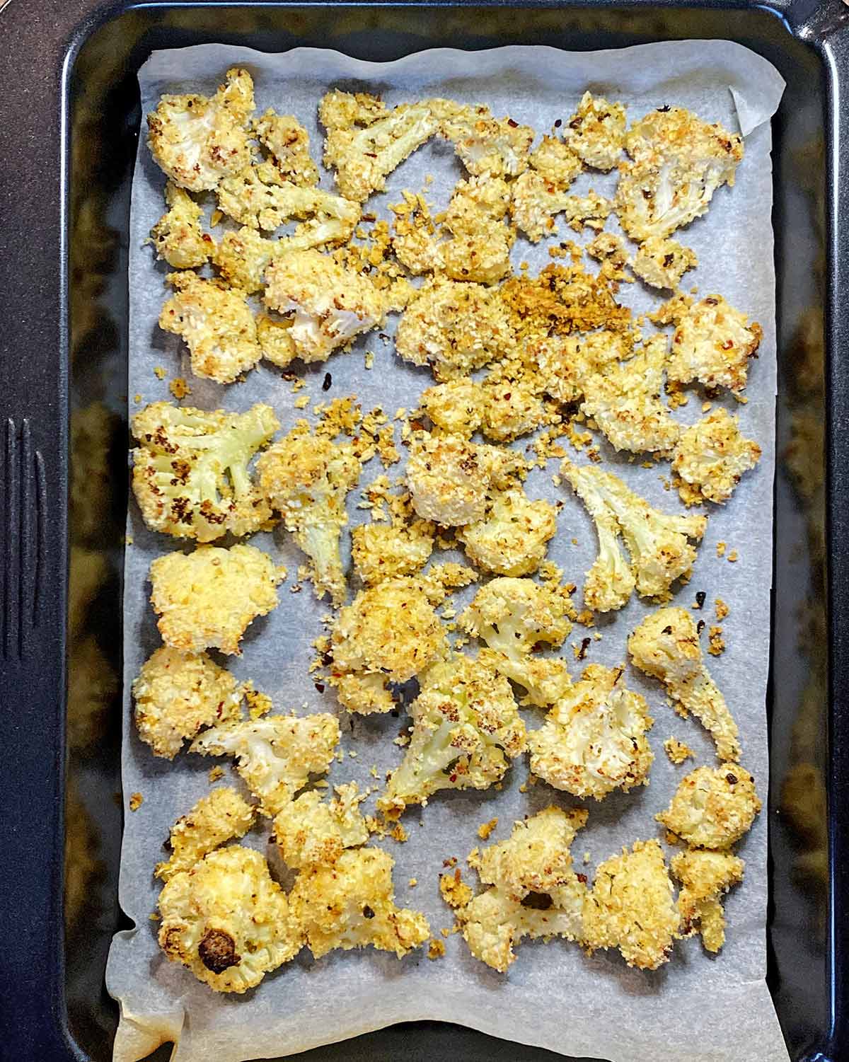 Cooked crispy cauliflower florets on a lined baking tray.