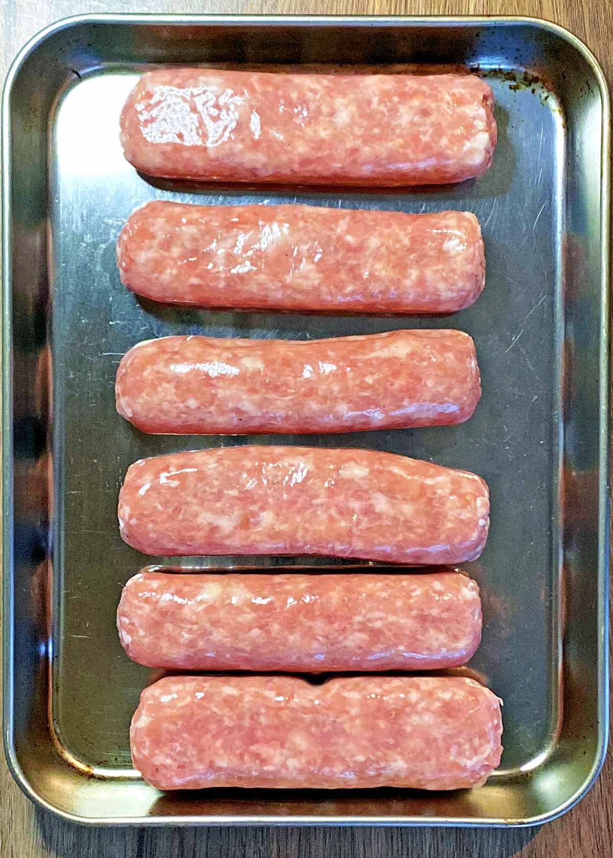 Six uncooked sausages on a baking tray.