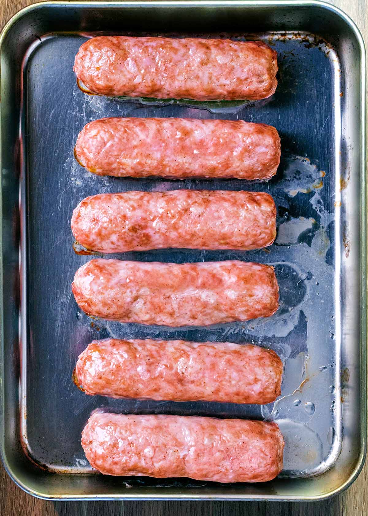 Six cooked sausages on a baking tray.