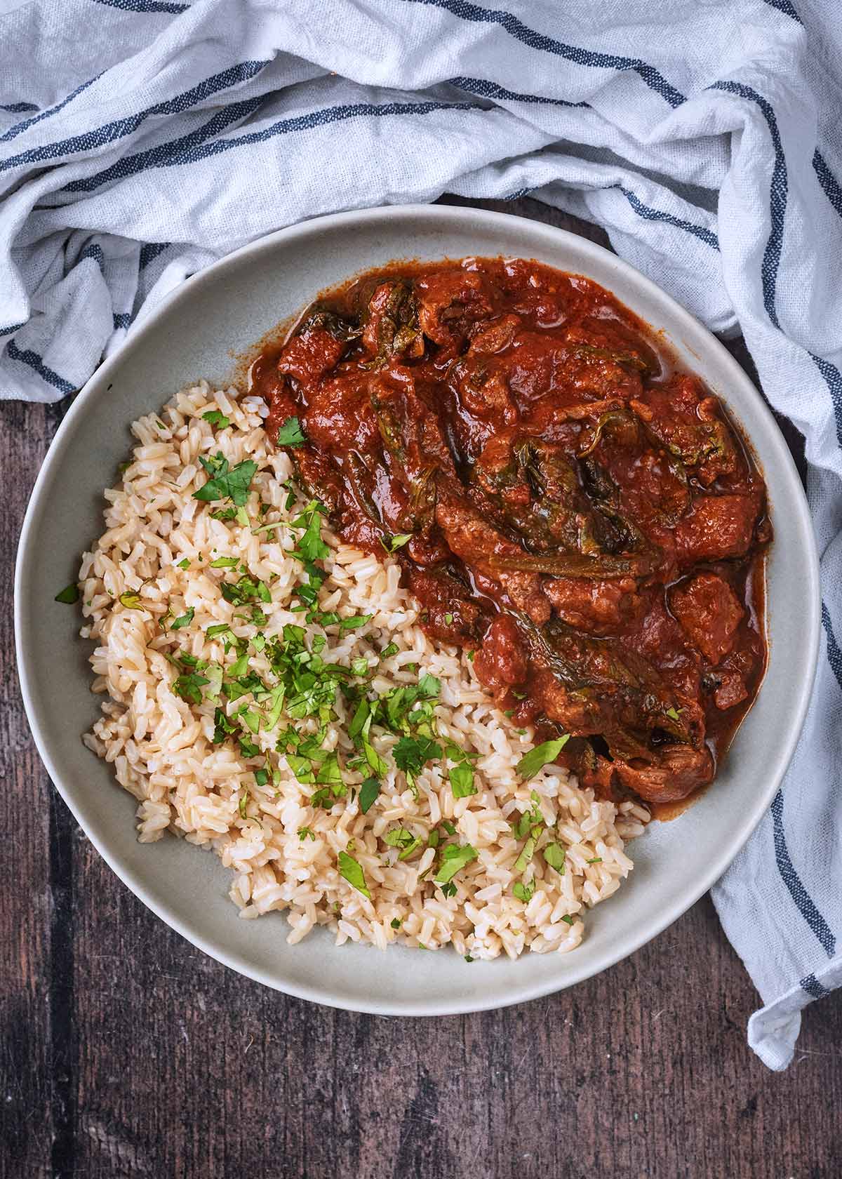 Beef curry and rice on a plate next to a striped towel.