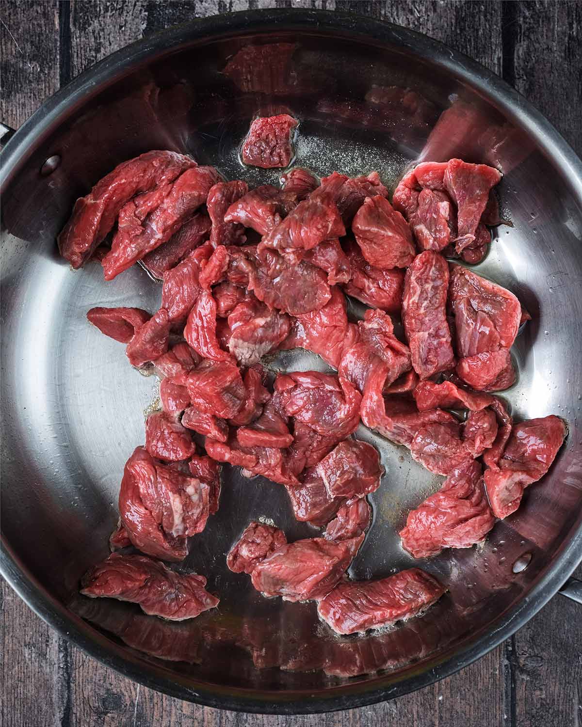 Chunks of beef cooking in a large pan.
