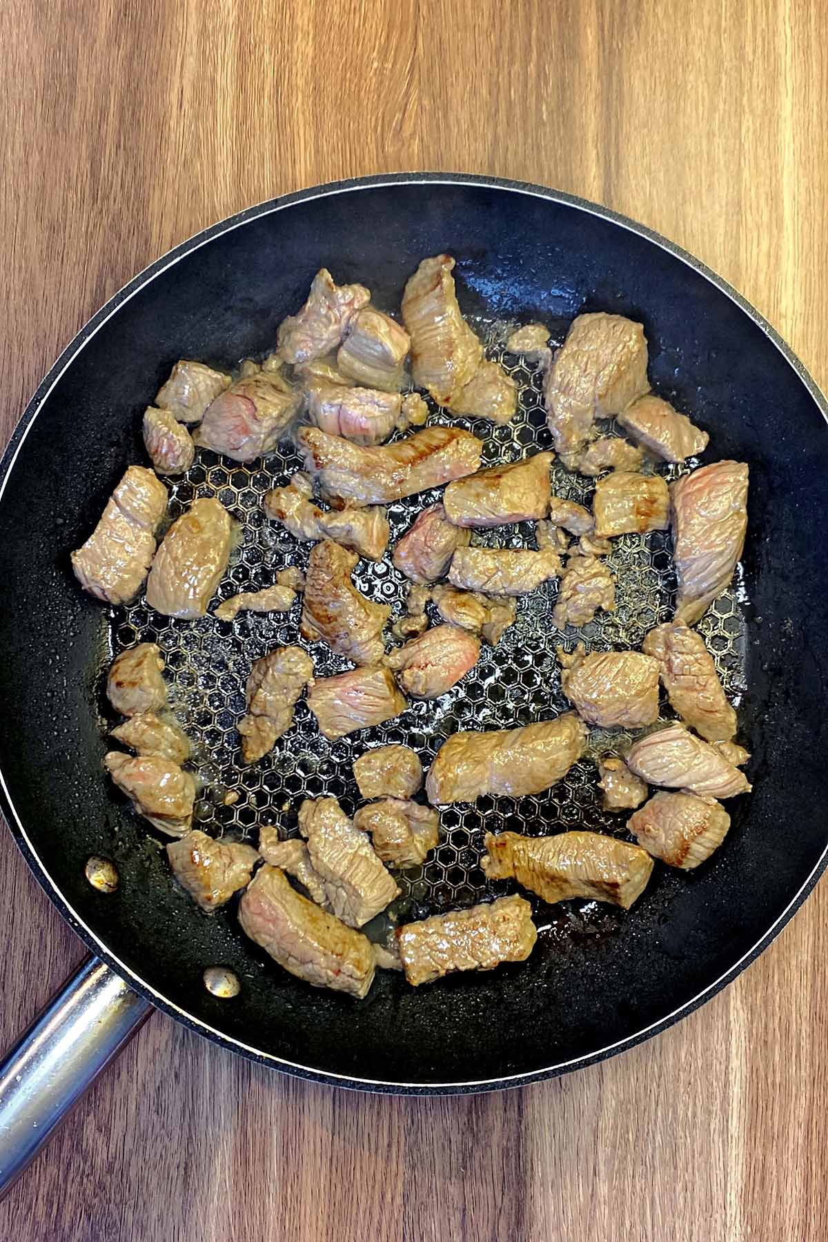 Chunks of browned beef in a frying pan.