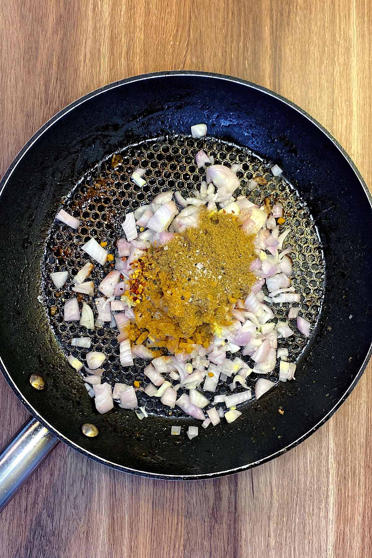 Chopped shallots and spices in a frying pan.