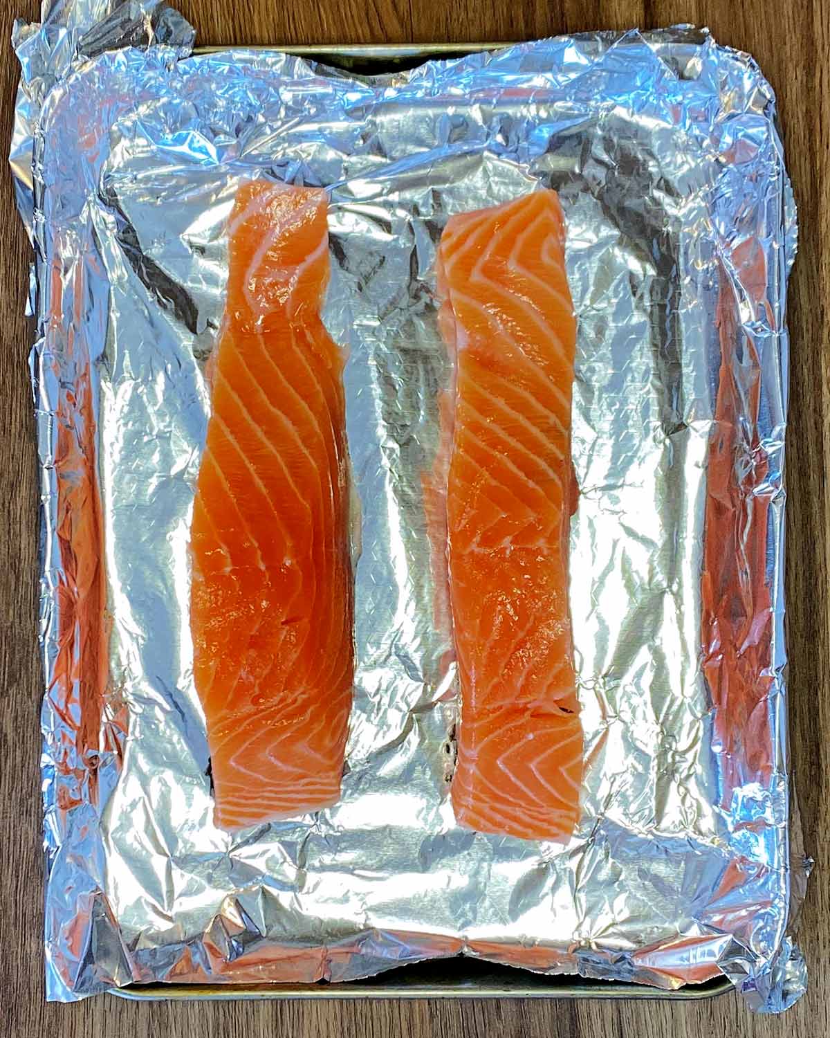 Two salmon fillets on a baking tray lined with foil.