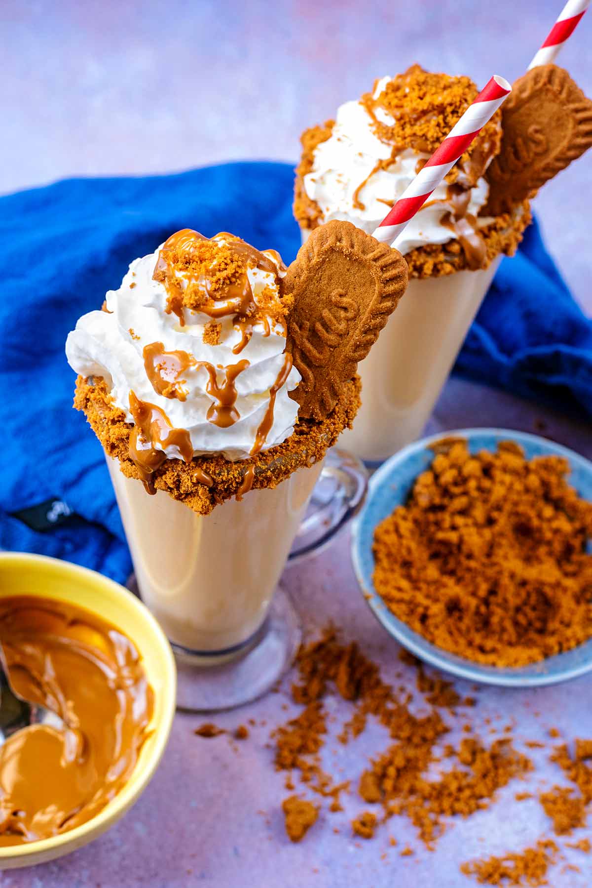 Two Biscoff milkshakes next to a bowl od Biscoff spread and crushed Lotus biscuits.