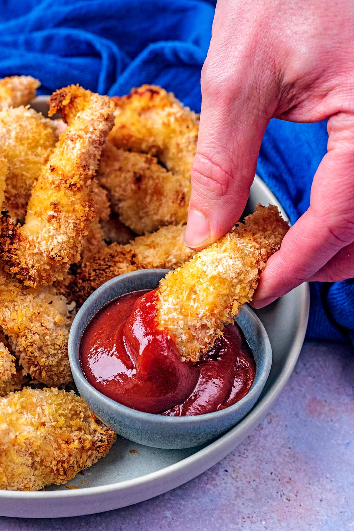 A hand dipping a chicken goujon into some ketchup.