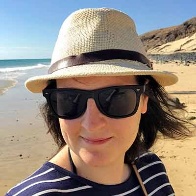Dannii in hat and glasses stood on a beach.