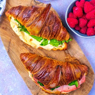 Ham and Cheese Croissants on a board next to some raspberries.