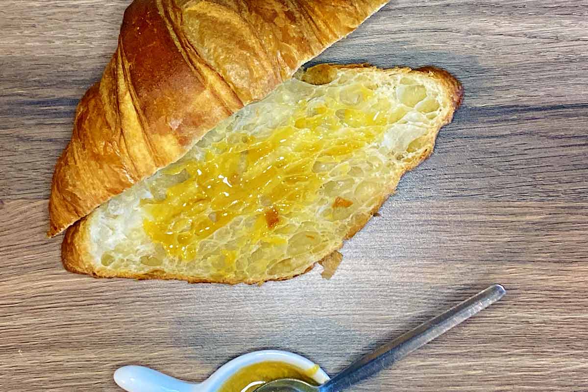 A croissant cut in half with the bottom spread with honey and mustard.