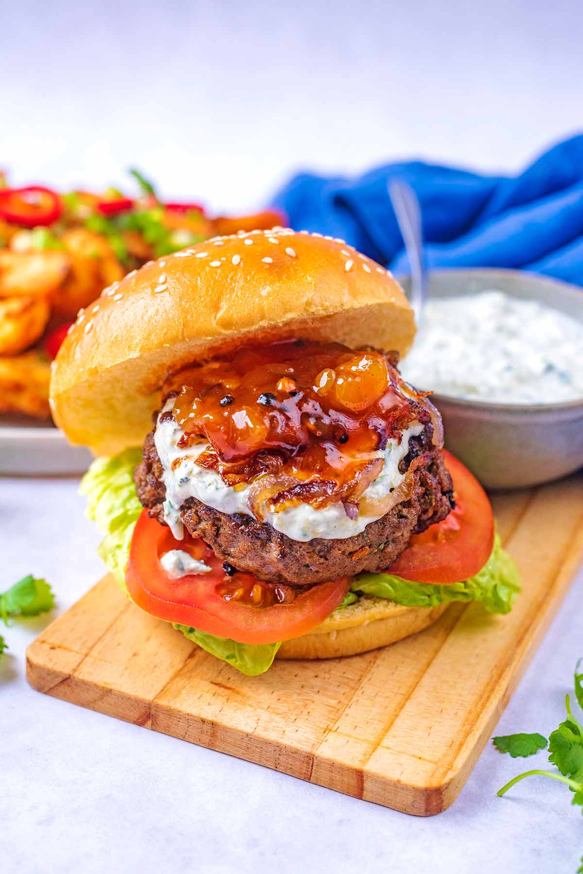 A stacked burger on a wooden board in front of a bowl of creamy sauce.