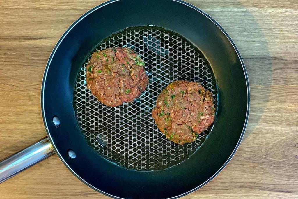 Two burgers frying in a pan.