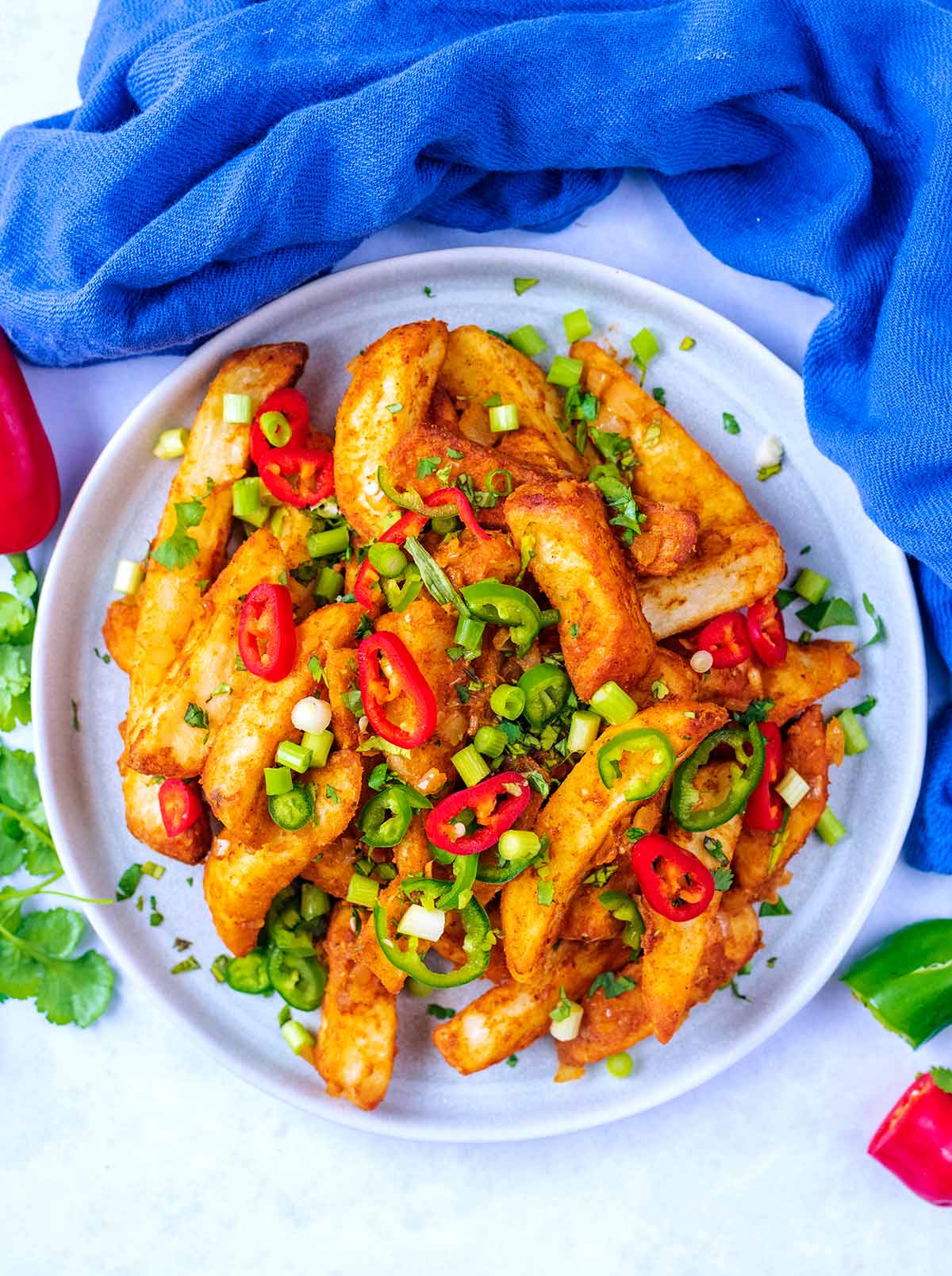 A plate of spiced chips topped with sliced chillies and spring onions.