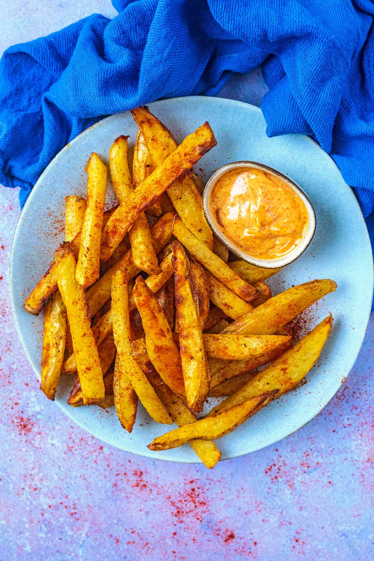 A plate of chips and a small bowl of dip on a round blue plate.