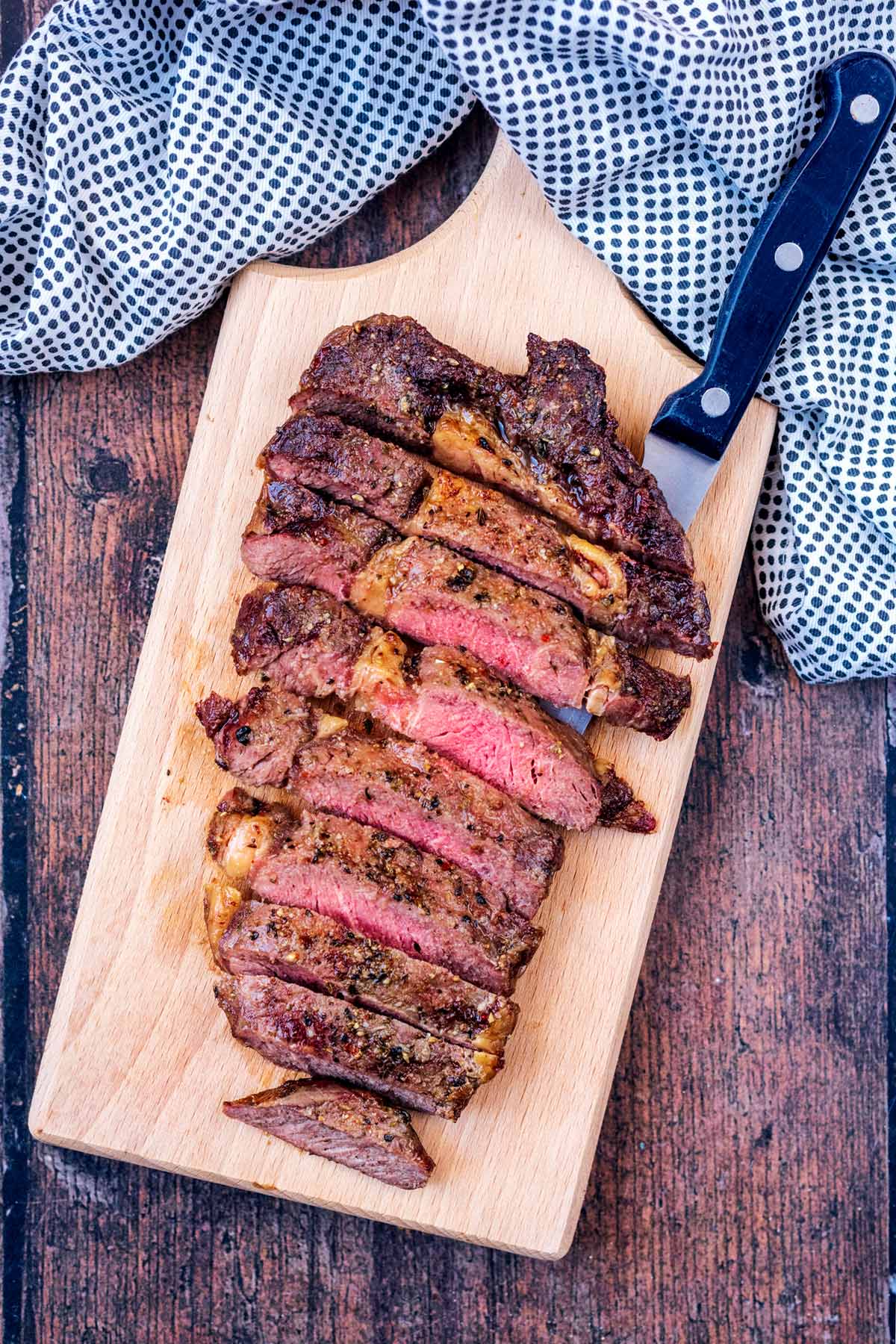 Strips of medium rare steak on a wooden serving board.