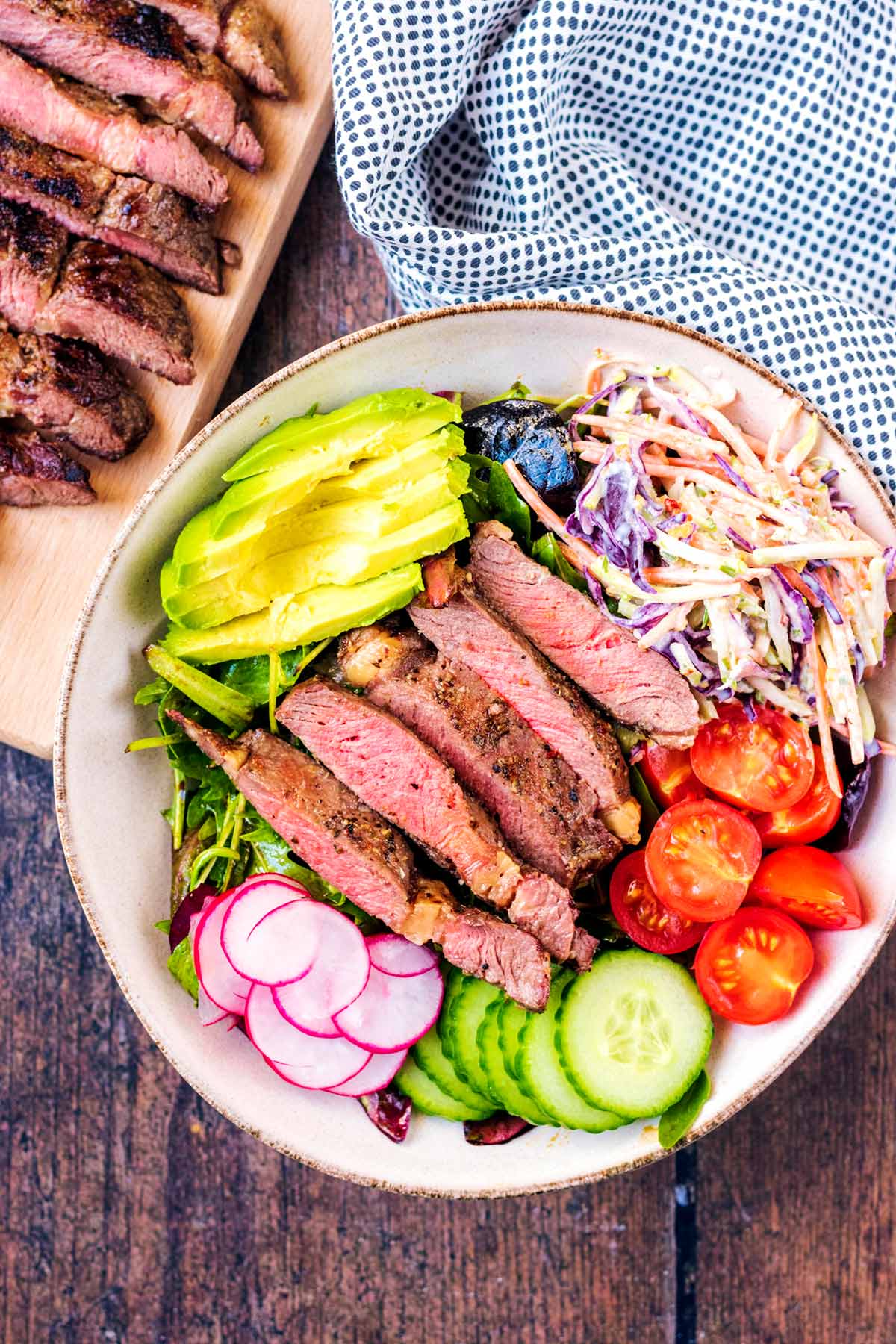 A bowl of salad topped with strips of medium rare steak.