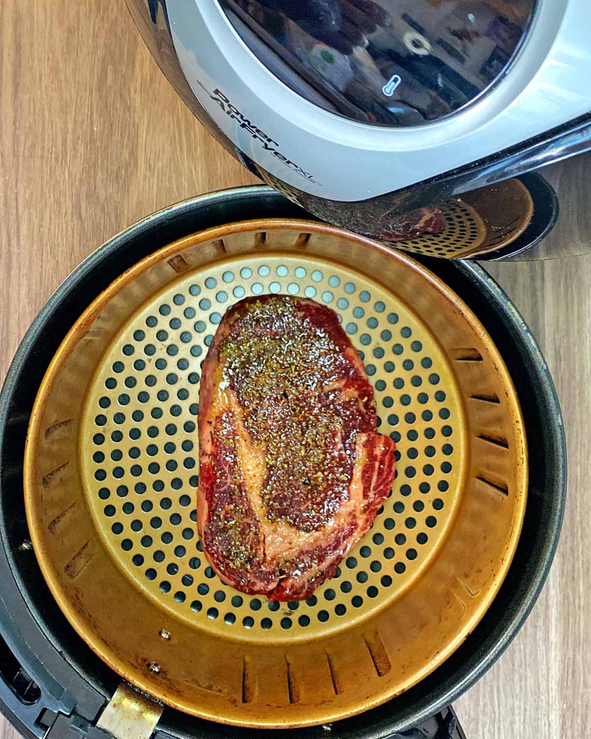 An air fryer basket with a seasoned ribeye steak in it.
