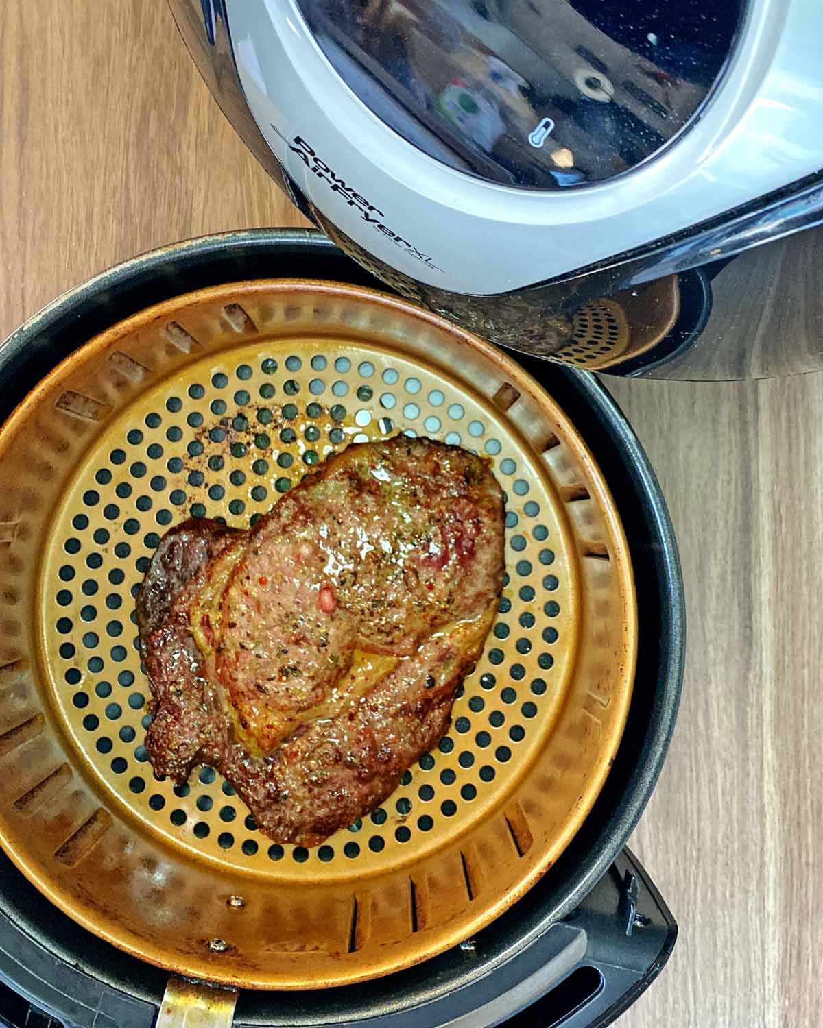 An air fryer basket with a cooked steak in it.