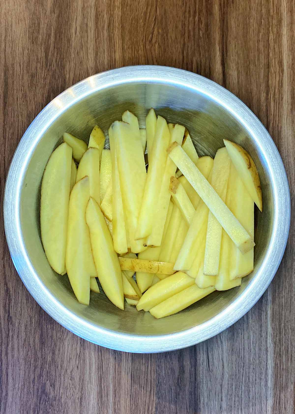 A metal mixing bowl full of uncooked chips.