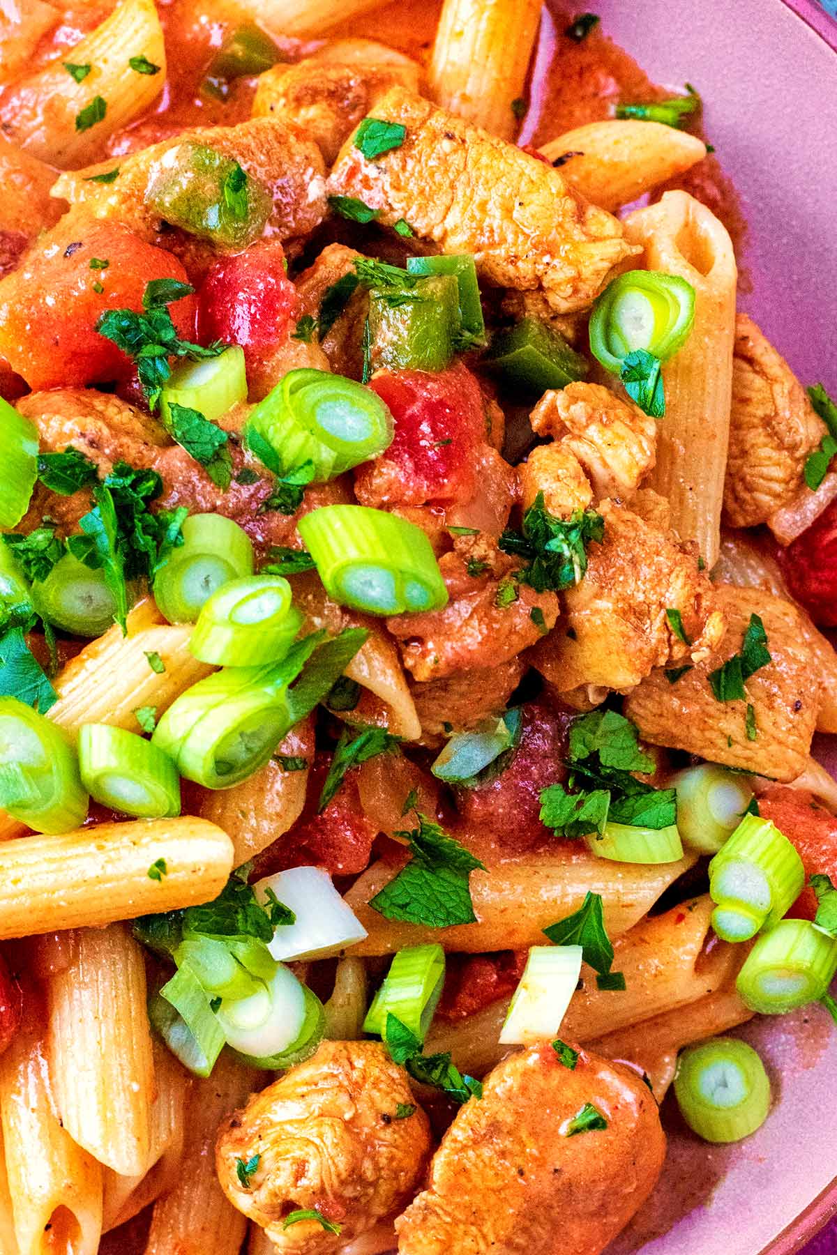 Green onions scattered over penne pasta and chicken in a tomato sauce.
