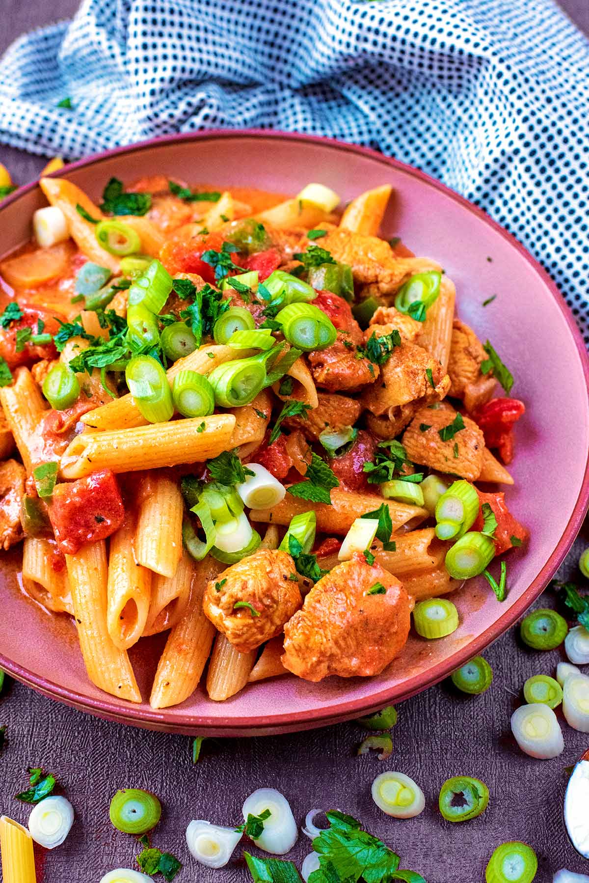 Penne pasta and chicken chunks on a plate, surrounded by chopped spring onions.
