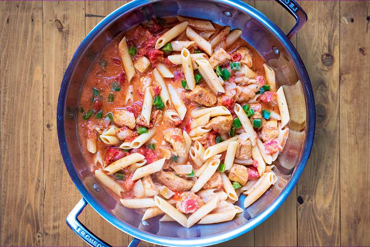 A creamy tomato chicken pasta dish cooking in a large silver pan.