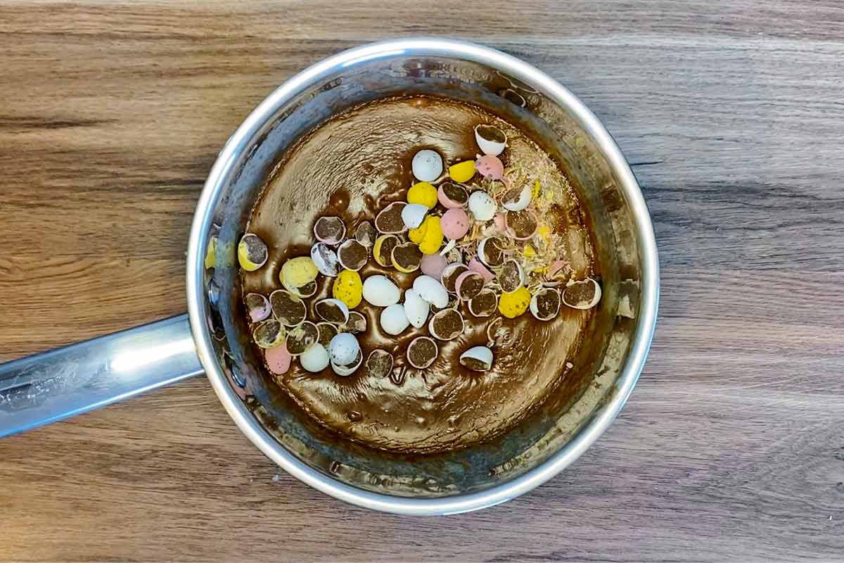 A saucepan containing melted chocolate and broken mini eggs.