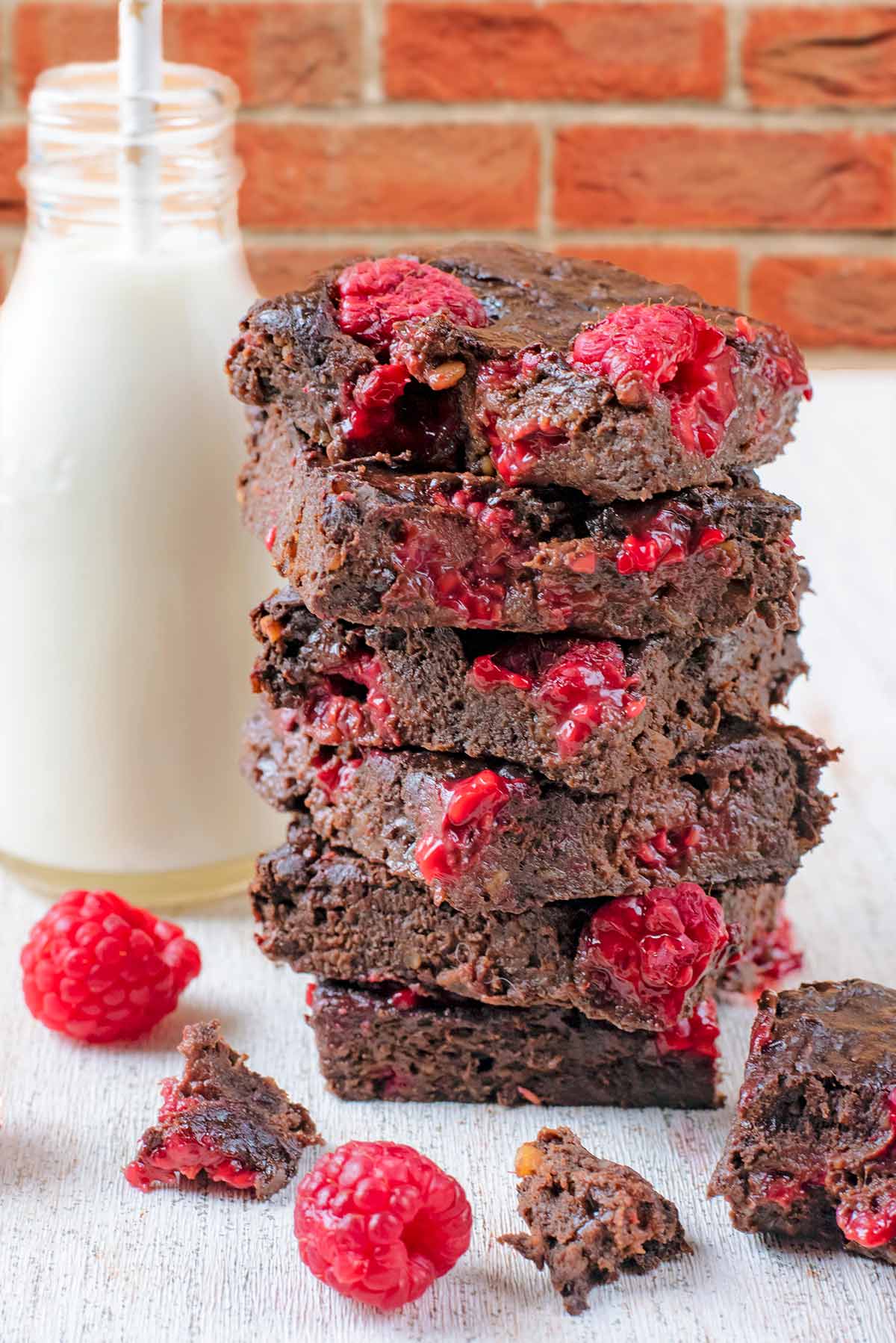 A stack of six chocolate raspberry brownies next to a bottle of milk.