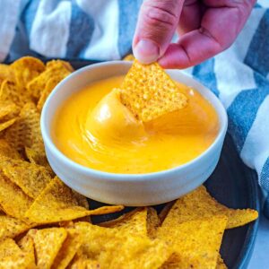 A tortilla chip being dipped into some nacho cheese sauce.