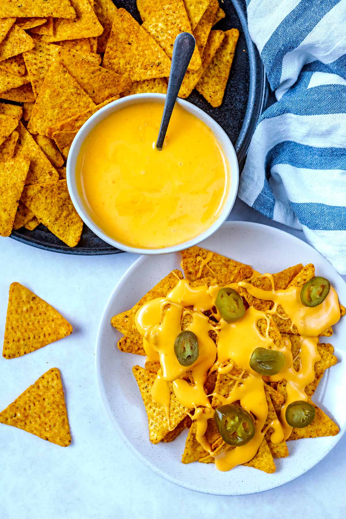 A plate of nachos covered in cheese sauce with a bowl of more sauce next to it.