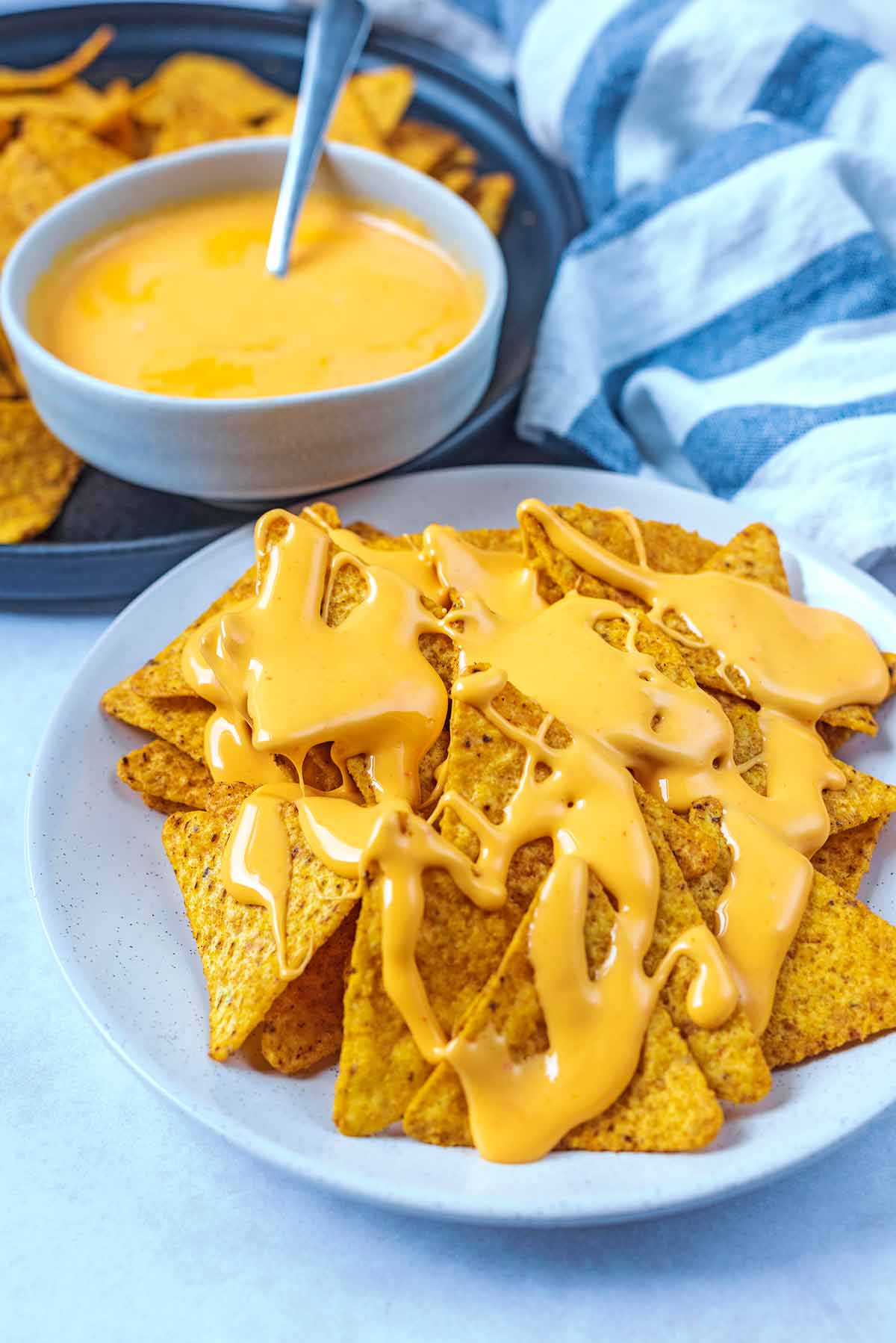 Tortilla chips smothered on nacho sauce with a bowl of sauce in the background.