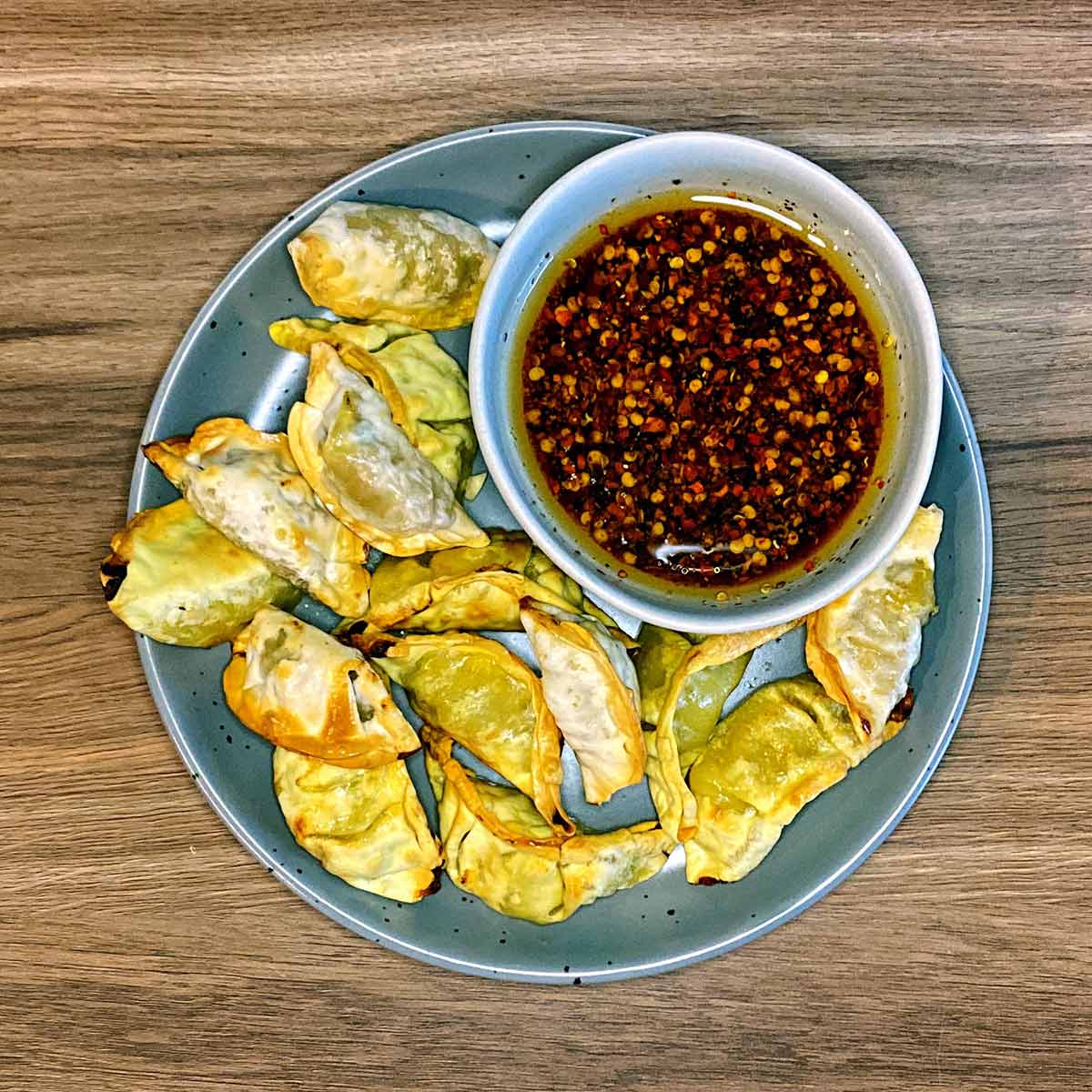 Cooked gyoza on a plate with a bowl of sauce.