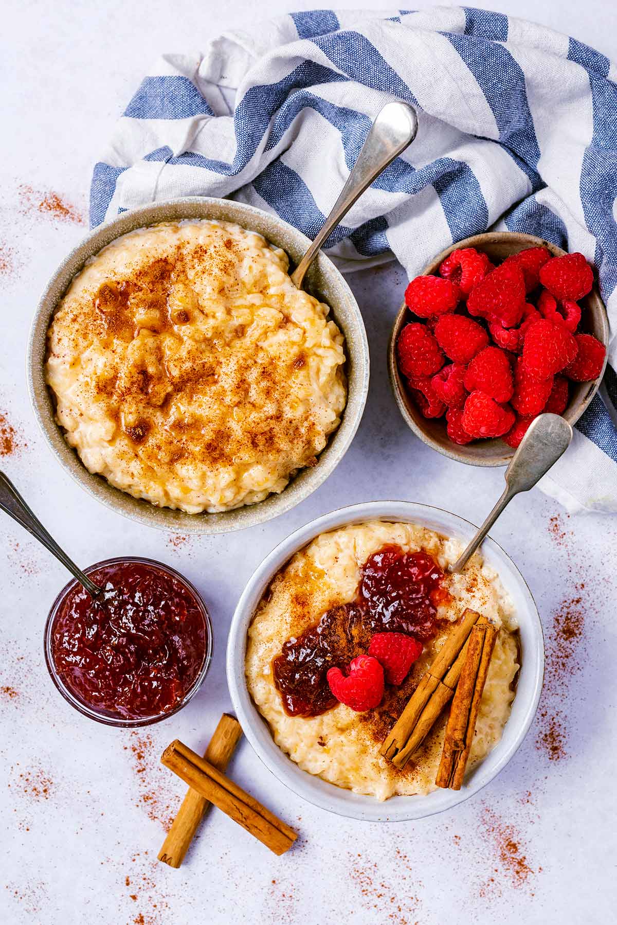 Two bowls of rice pudding one topped with cinnamon, one topped with jam.