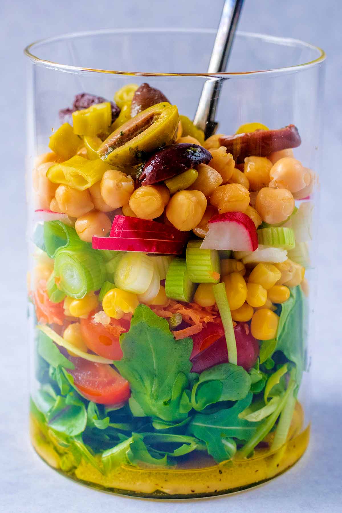 Layers of salad items in a jar with a fork.