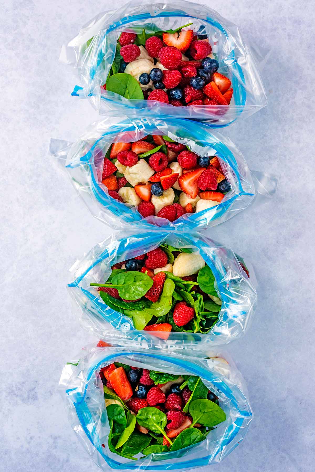 Four open ziploc bags with berries and spinach in them.