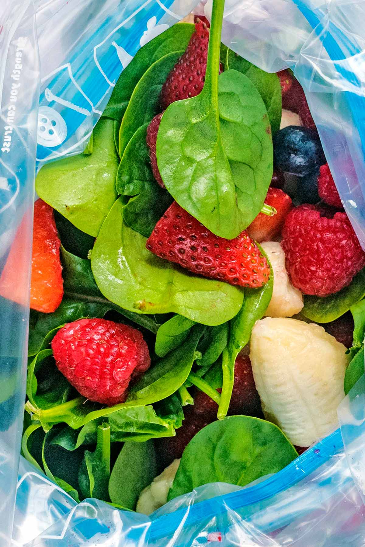 An open ziploc bag showing spinach leaves and berries.
