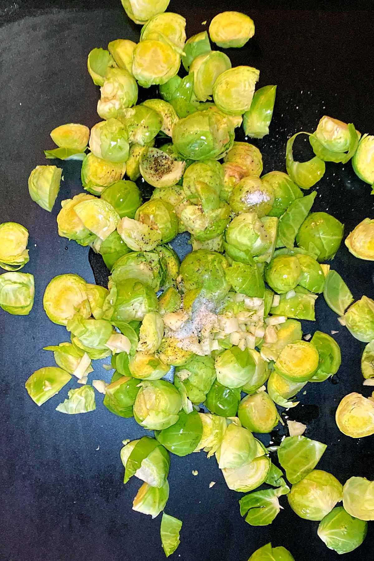 Chopped Brussels sprouts, garlic, oil, salt and pepper on a baking tray.