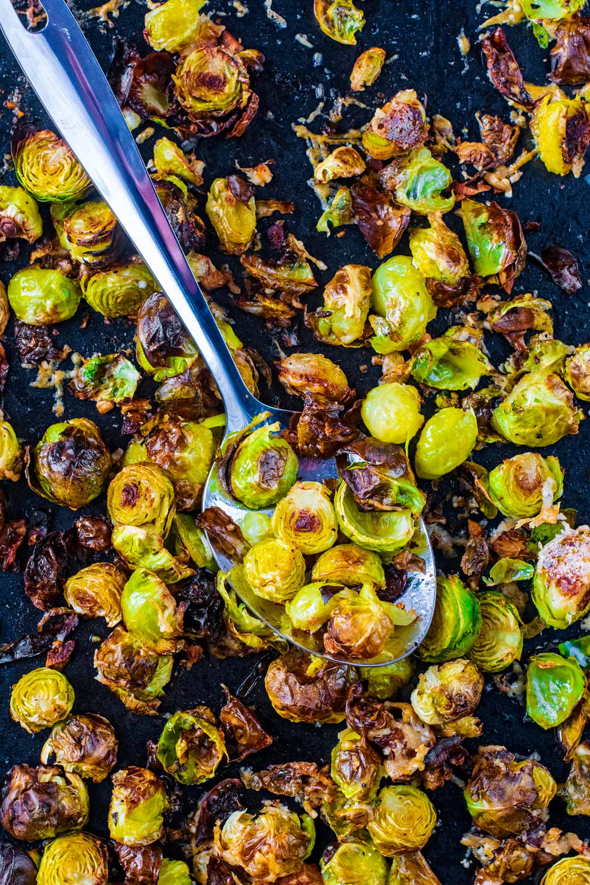 A baking tray covered in cooked Brussels sprouts with a large serving spoon.