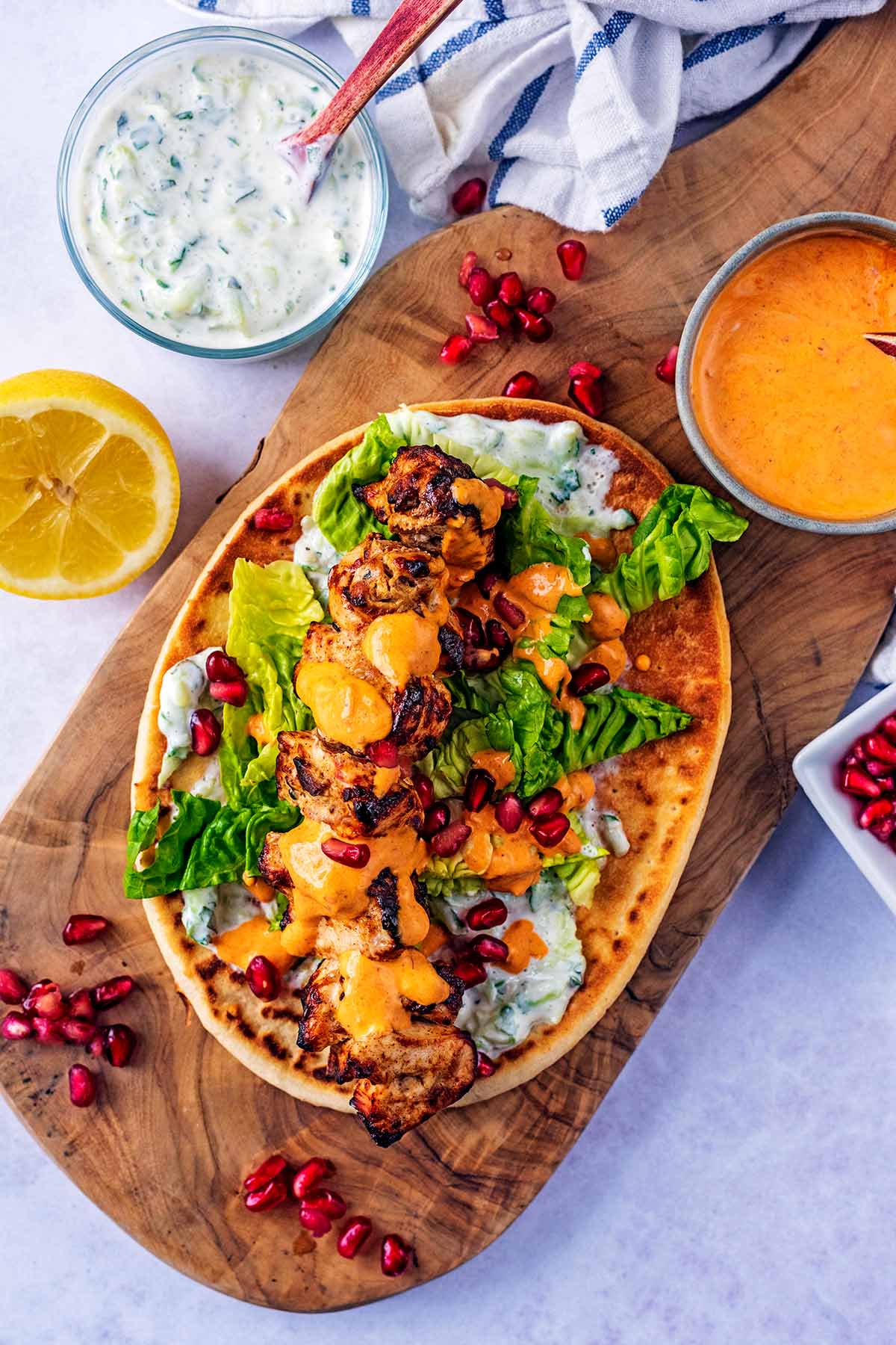 A flatbread topped with lettuce, cooked chicken, tzatziki and pomegranate seeds.