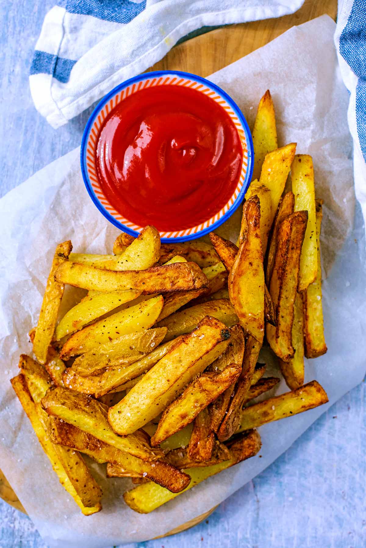 Air Fryer Chips on a wooden serving board with a small pot of ketchup.