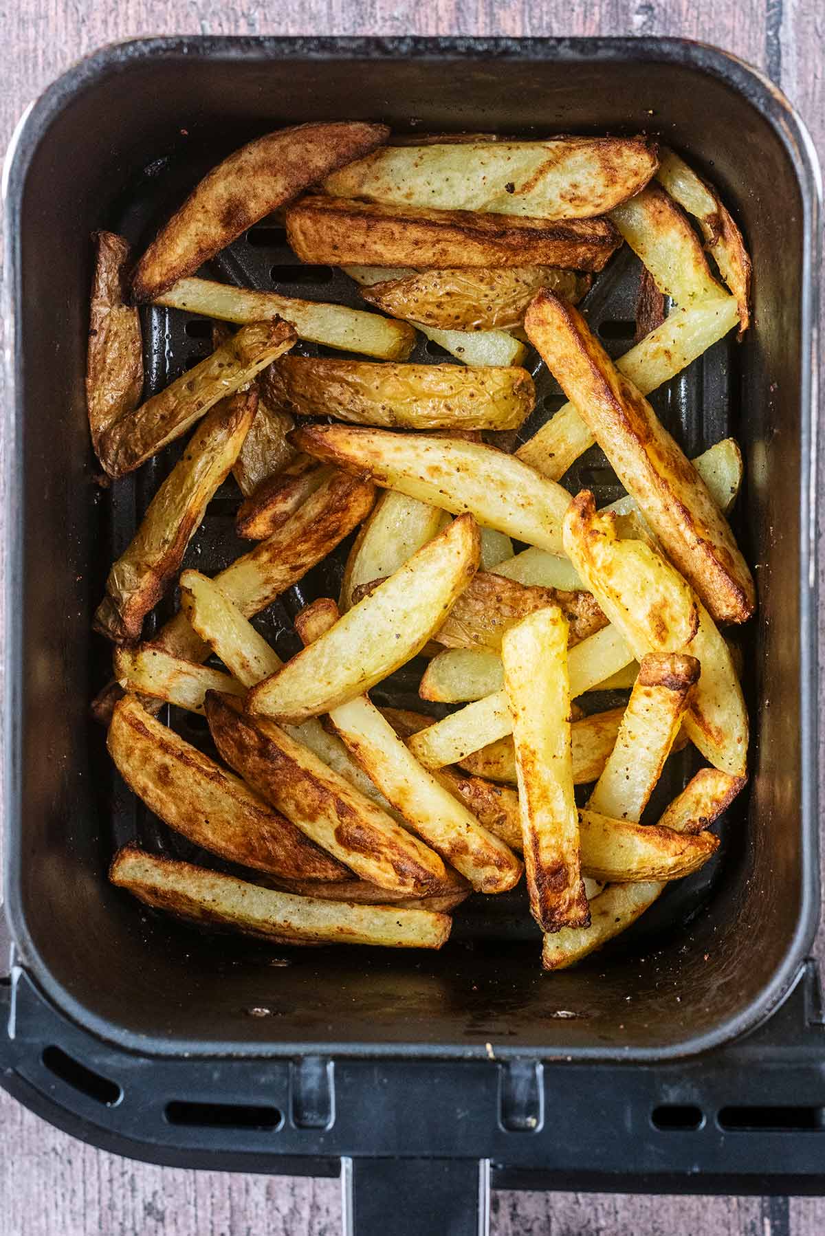 Cooked chips in an air fryer basket.