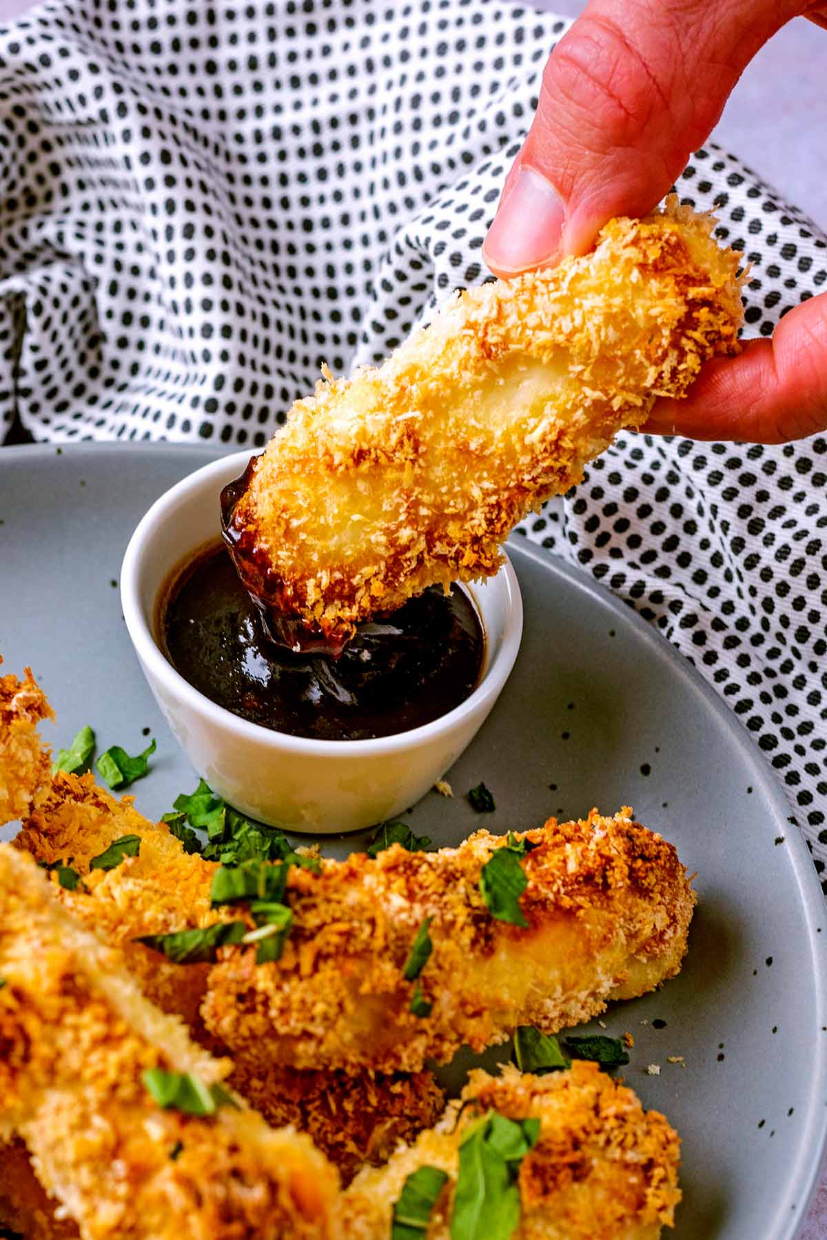 A halloumi fry being dipped into a small pot of barbecue sauce.