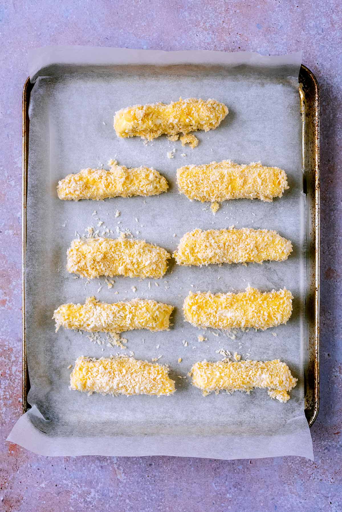 Uncooked halloumi fries on a lined baking tray.