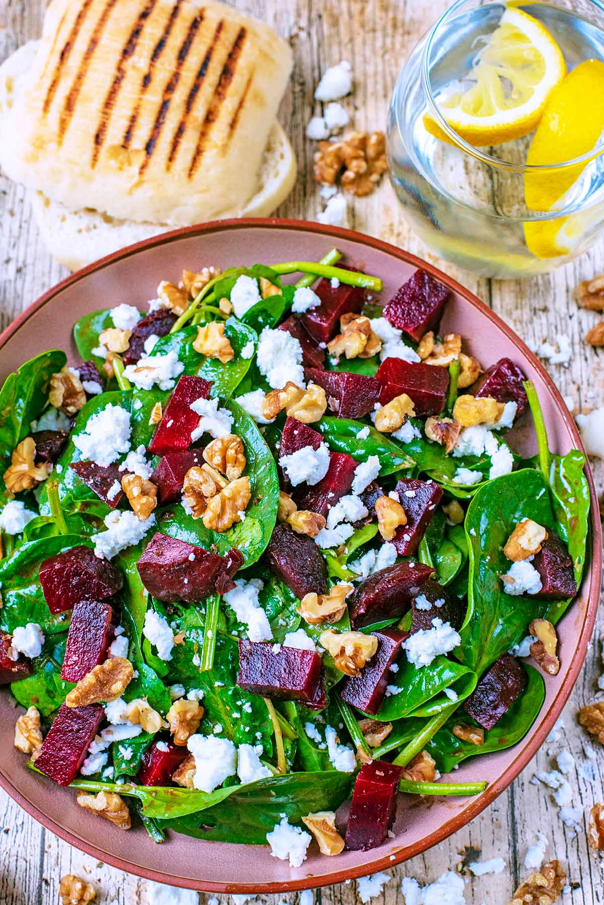 A bowl of Beetroot and goat's cheese salad, next to a ciabatta and a glass of water.