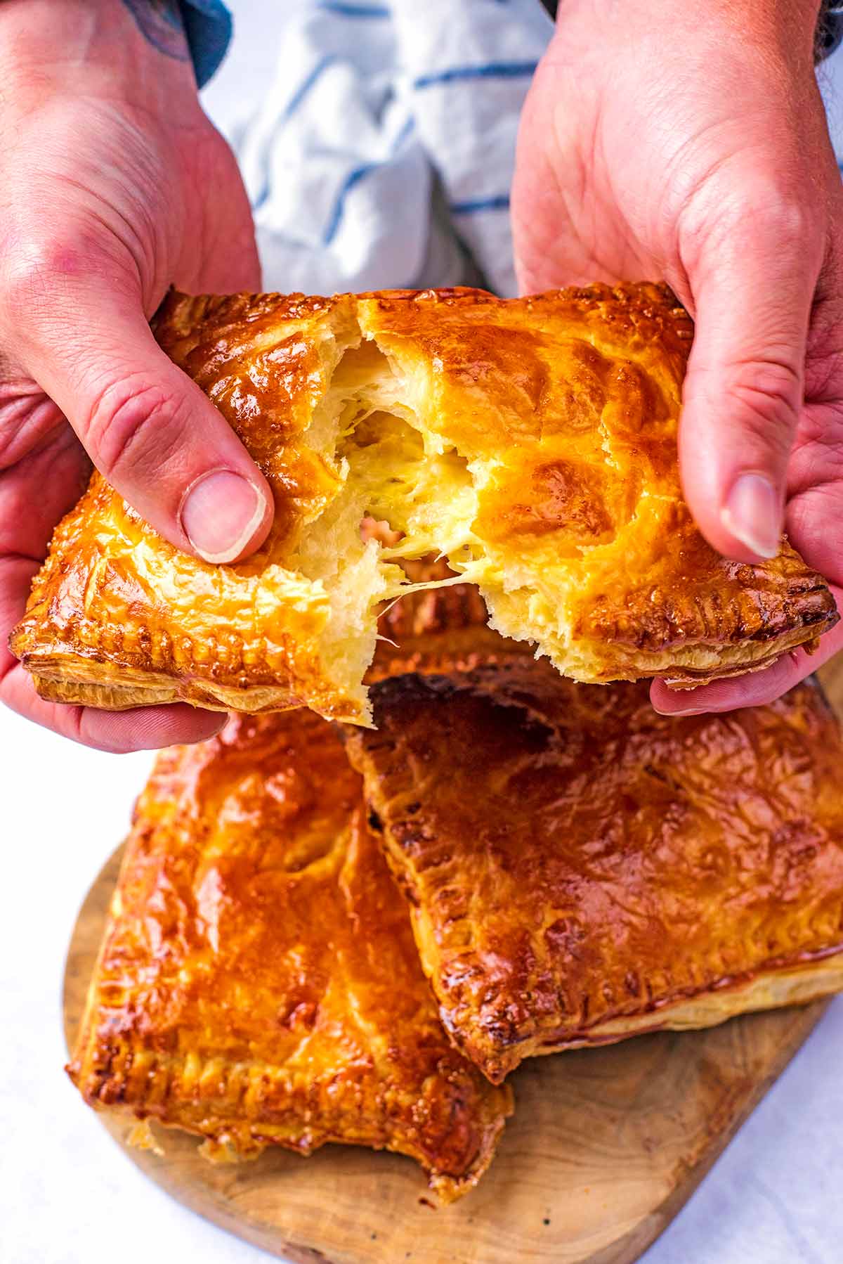 Two hands pulling apart a cheese and onion pasty showing the filling.