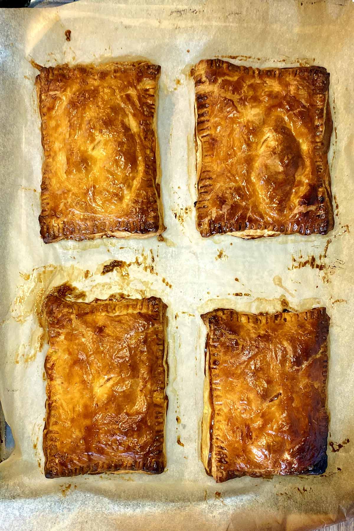 Four golden brown cheese and onion pasties on a baking tray.
