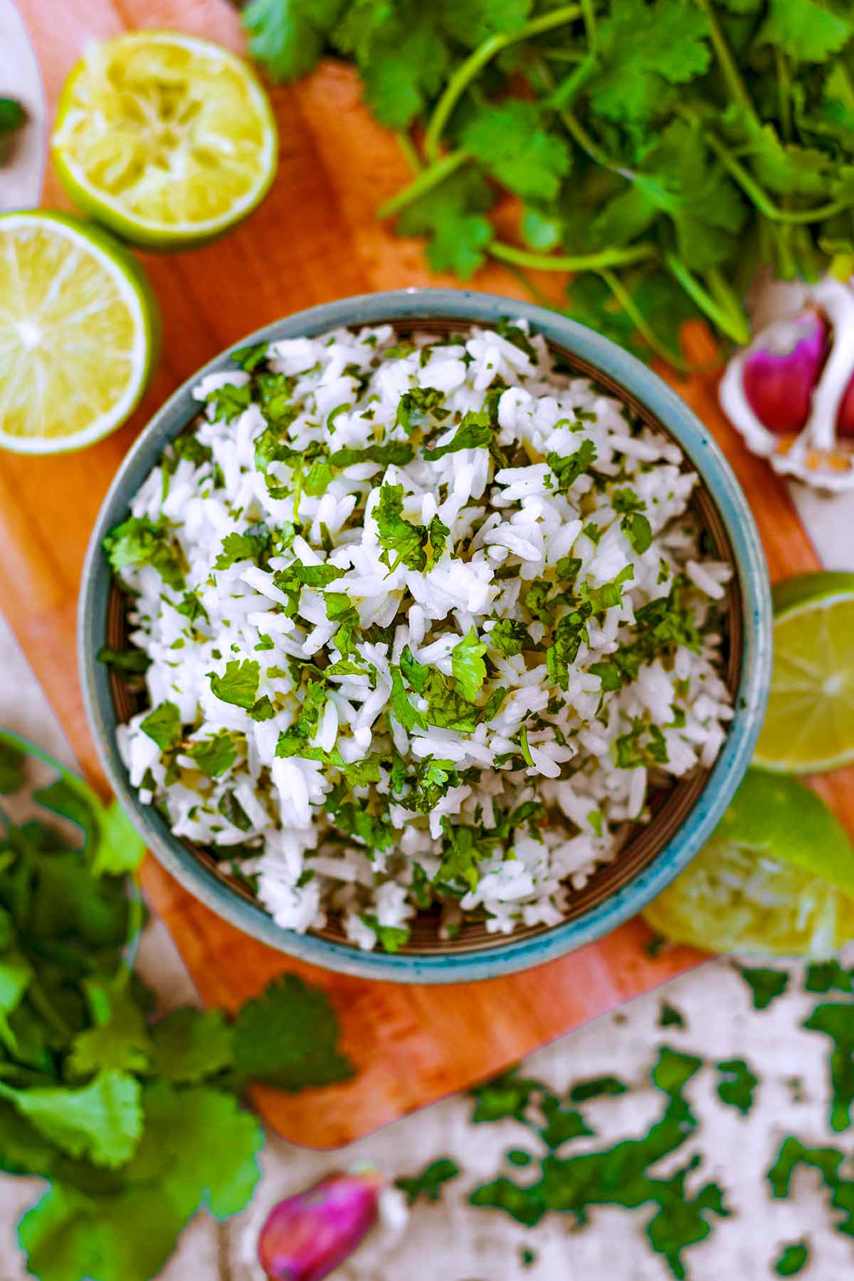 A bowl of cilantro lime rice surrounded by more cilantro and lime halves.