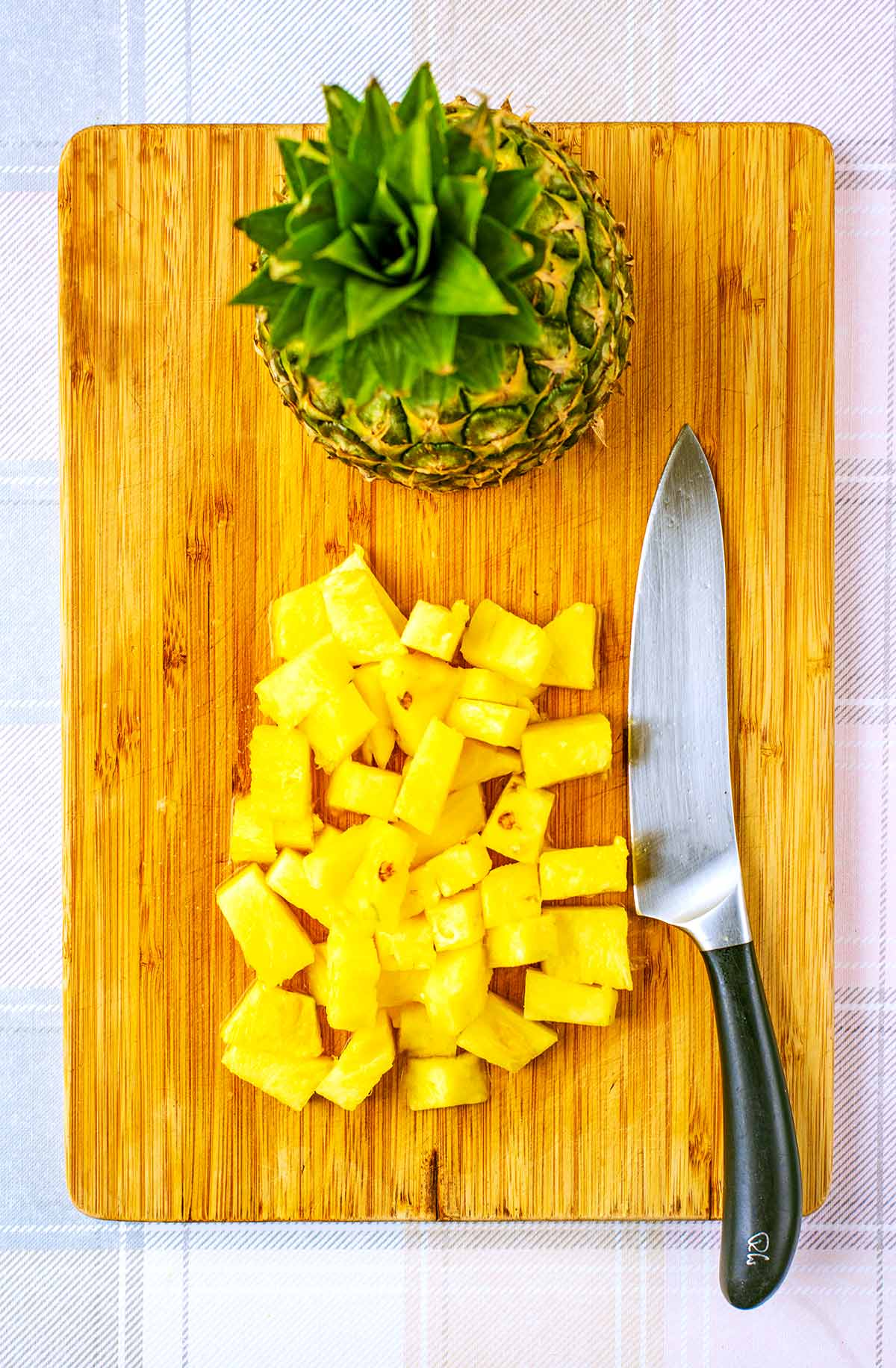 a wooden chopping board with a chef's knife, chunks of pineapple and a half whole pineapple.