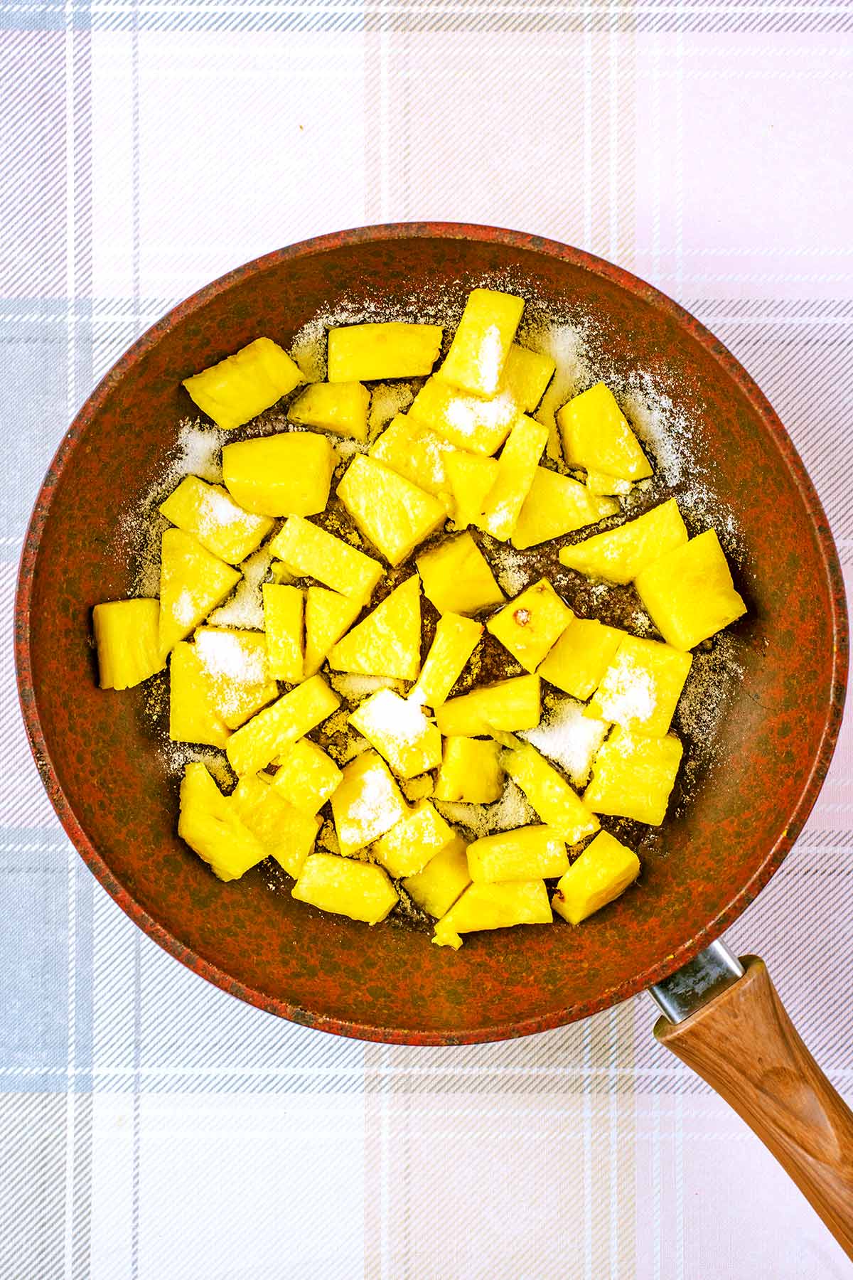 a frying pan containing chunks of pineapple and sugar.